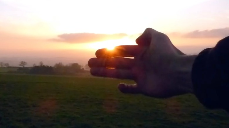 A hand held up to the setting sun to measure how much daylight is left