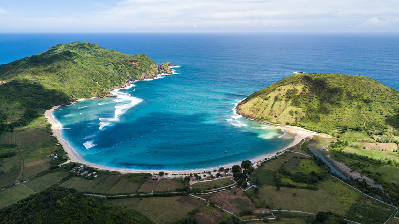 Horseshoe-shaped bay surrounded by green hills and blue water in Mawun Beach in Lombok, Indonesia