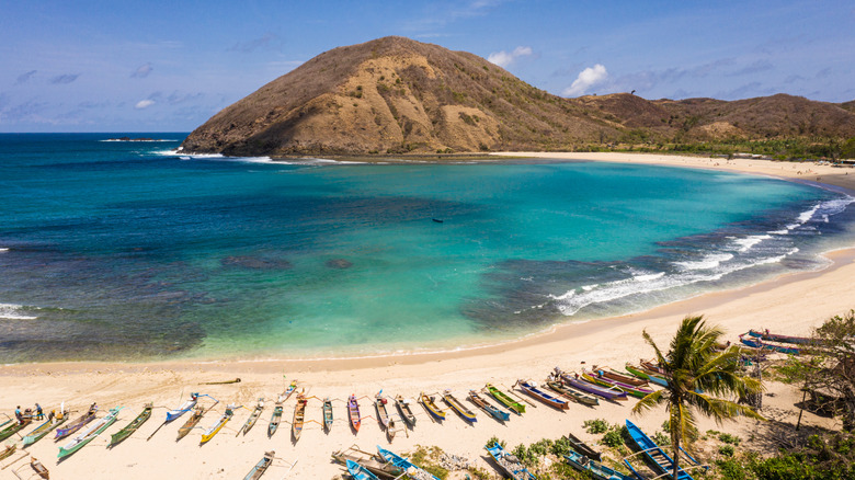 Boats on sand, emerald water, towering hill in Mawun Beach in Lombok, Indonesia