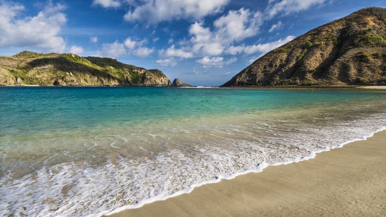 Cloudy blue sky above two hills towering over emerald water in Mawun Beach in Lombok, Indonesia