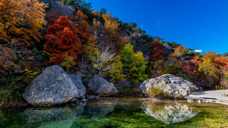 Crystal-clear water with reflections of boulders surrounded by fall foliage