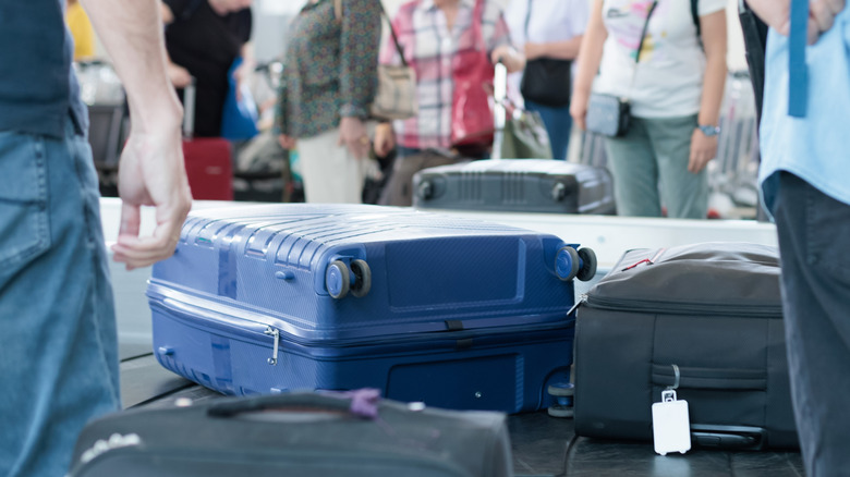 Suitcases coming out onto a baggage carousel at an unidentified airport, with many passengers standing around and waiting in the background.