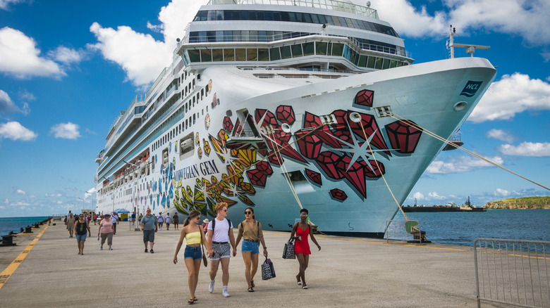 Young people walk outside docked cruise ship with blue sky and clouds