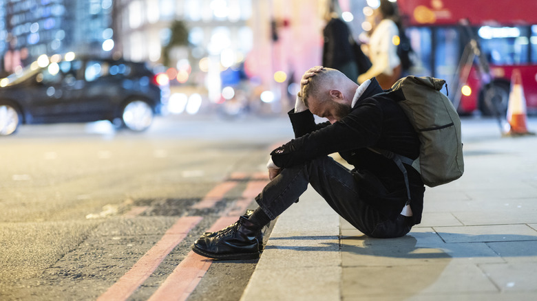 Man with backpack sat on sidewalk with head in hands