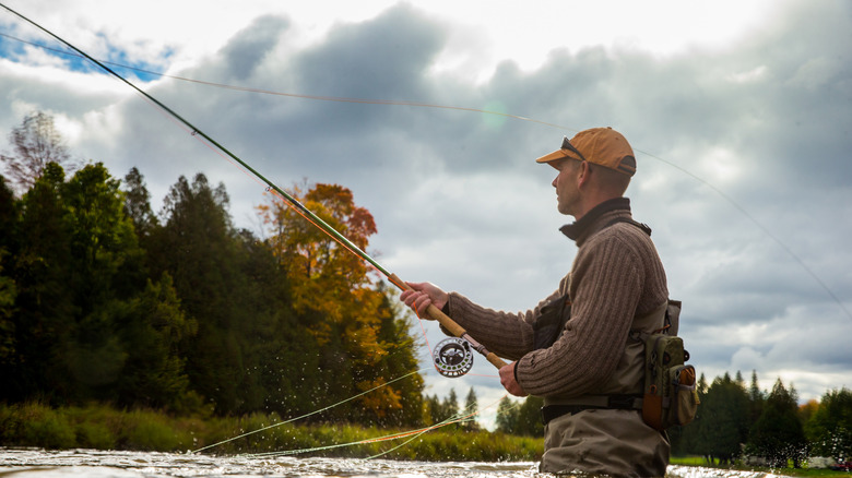A man fly fishes in a river in the fall