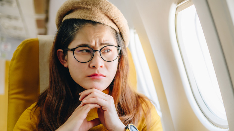 Woman sitting in a plane seat looking out the window with a worried expression