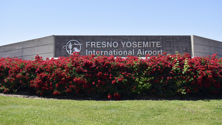 Red flowers grow in front of the sign for Fresno Yosemite International Airport.