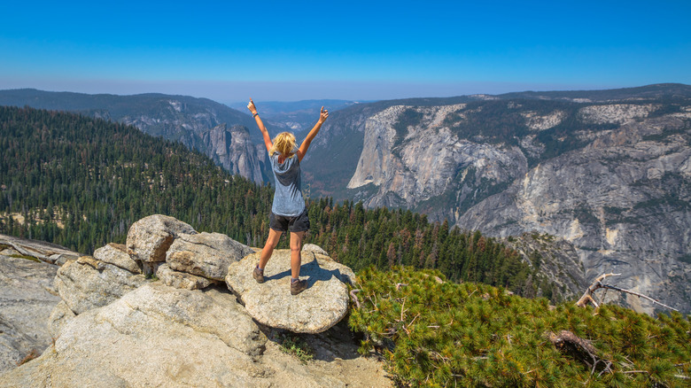 hiker standing at summit of Sentinel Dome, overlooking forest and valley in Yosemite