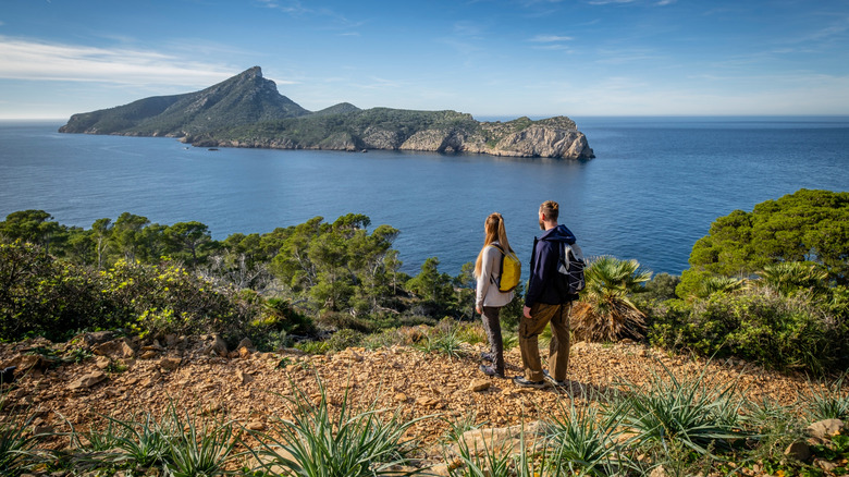 Couple standing on a rocky cliff overlooking the sea, with an island in the distance, Mallorca
