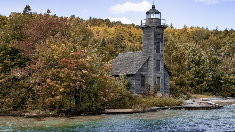 A historic wooden lighthouse on the shore with fall foliage