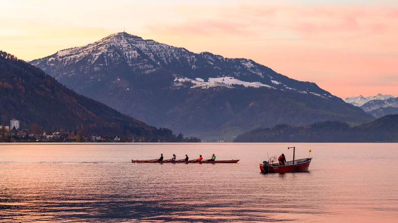 A sunset behind a snowy mountain on Lake Zug with rowers and a fisherman