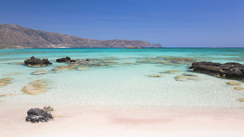Pink sand and a turquoise sea with red rocks behind