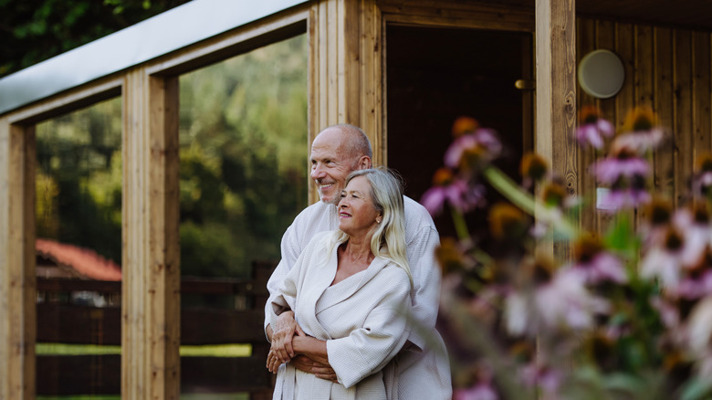 older couple embracing outside of sauna in robes