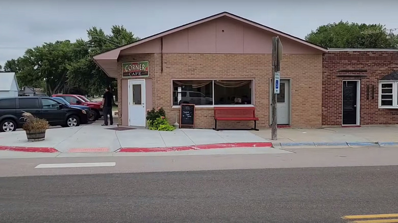 A small corner cafe in a small town, with the building made from brick and a red bench in front