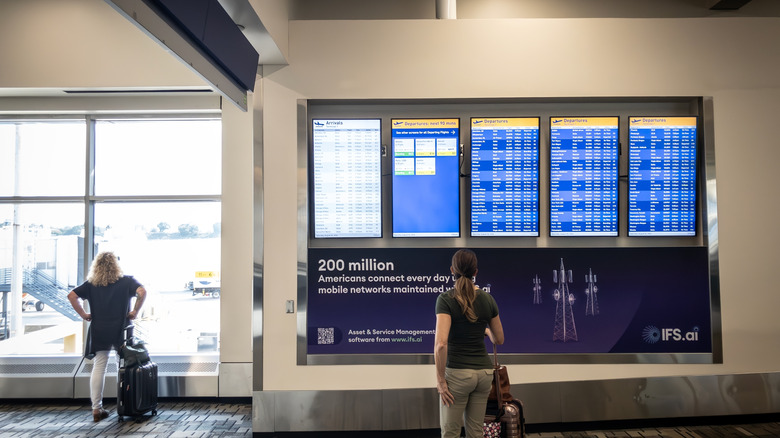 Passengers looking out the window and at the arrival and departure listings at MSP airport