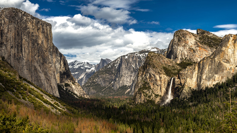 Tunnel View in Yosemite National Park showing snow-dusted mountains like Half Dome and El Capitan, evergreen forest covering the valley floor, and Bridalveil Fall