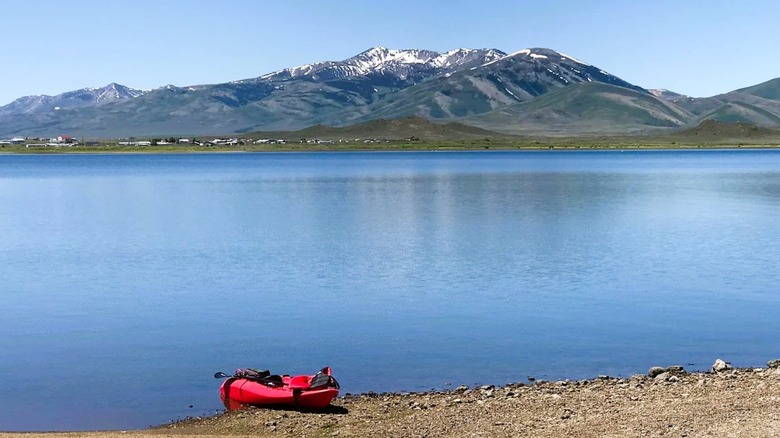 A kayak on the shoreline of Wild Horse Reservoir in Nevada, featuring a glass-like surface with snow-capped mountains in the backdrop.