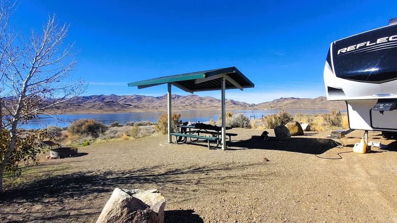 Partial view of an RV at a waterfront campsite at Wild Horse State Recreation Area in Nevada, featuring a shaded picnic area and a fire pit.