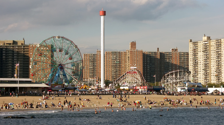 Coney Island rides seen across the water and beach with some clouds