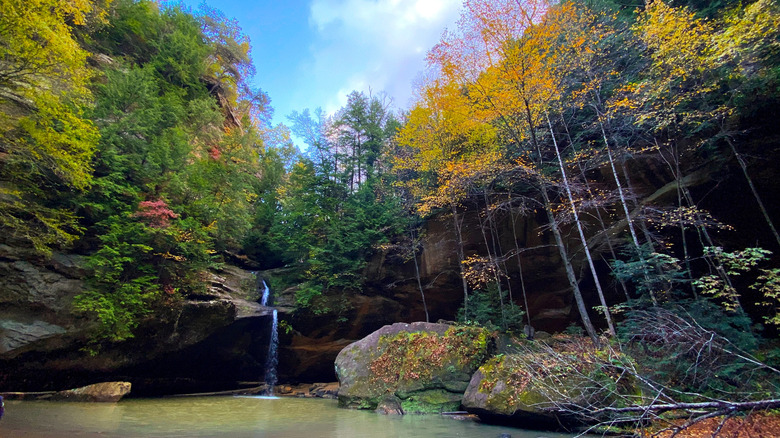 Waterfall in Hocking Hills State Park, with a pool in the foreground, blue sky above, and trees with yellow, red, and green leaves