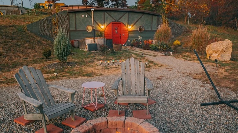 Hobbit Hole style home in Hocking Hills, with a red door, gray walls, and wooden adirondack chairs in the foreground