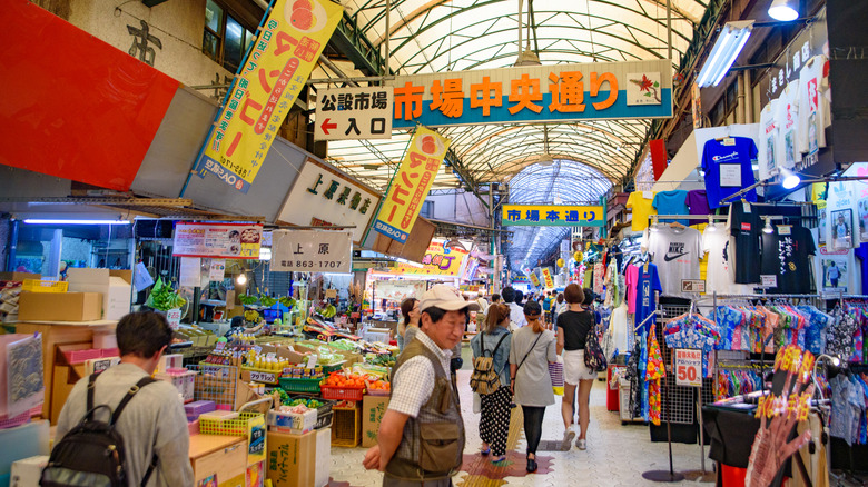 Tourists walking past colorful signs, fresh produce, and boutiques in Naha's Makishi Public Market