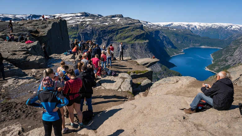 A large group of tourists lining up at the Trolltunga hiking summit in Norway waiting to take photos