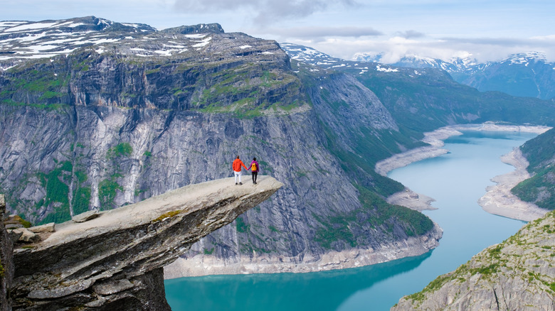 Two hikers standing at the ledge of Trolltunga in Norway overlooking fjords and water down below them