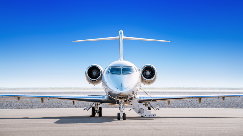 A private jet sits on a runway, ready for boarding, with a bright blue sky in the background
