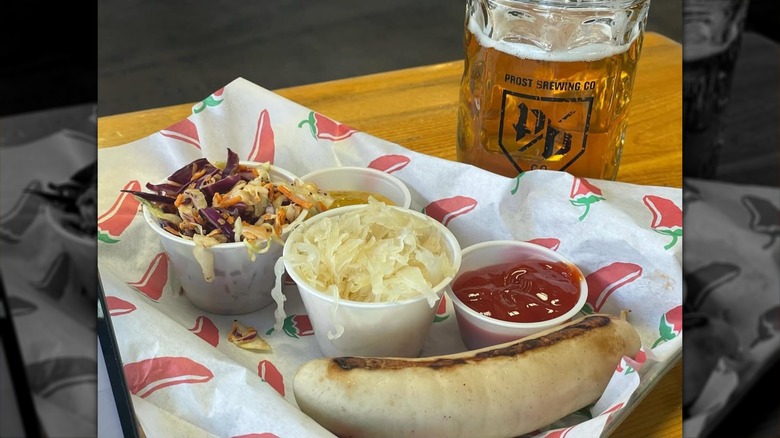 Table with a plate of sausage and a beer served in a Prost Brewing Co. glass.