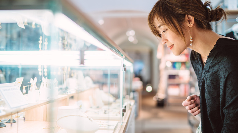 Woman with black top and dangling earrings gazing into the display at a jewelery shop