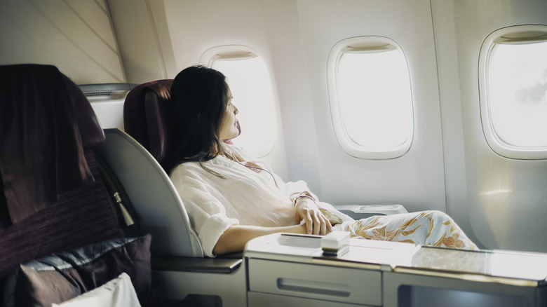 a woman relaxes by the window in her lie-flat seat in business class