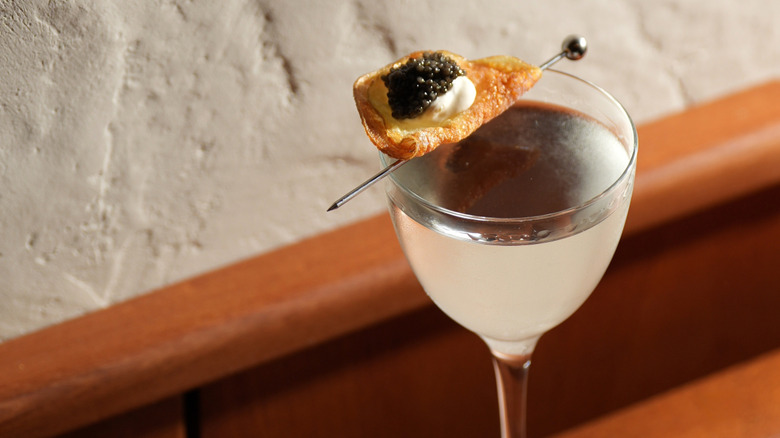 A martini garnished with a spoonful of caviar atop a potato chip