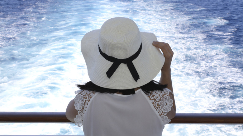 A woman wearing a hat looking out to sea from a cruise ship