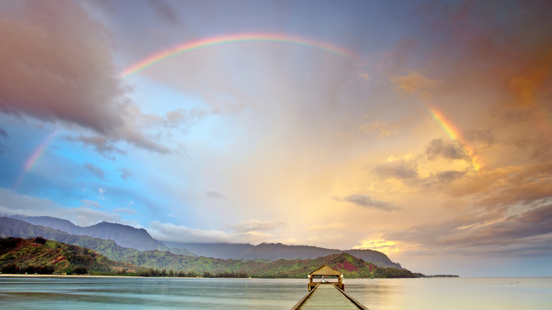 A rainbow appears above a pier on Kauai at sunrise