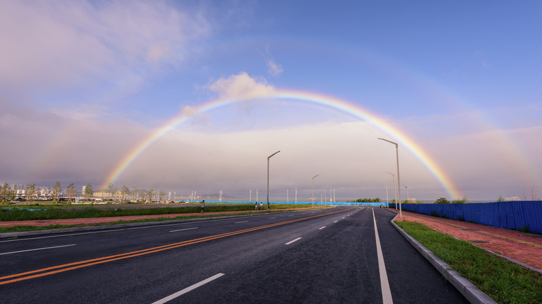 A double rainbow arches above a city road at sunset