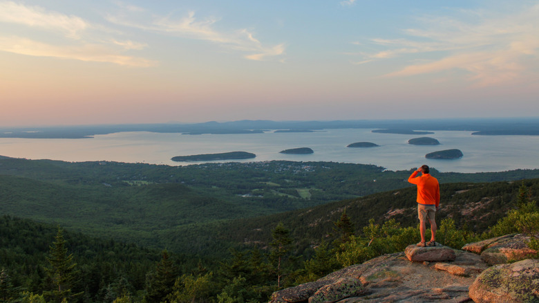 A hiker on Cadillac Mountain overlooking islands, ocean, and forest in Acadia National Park, Maine