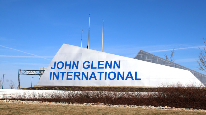 A large sign for John Glenn Columbus International Airport in Ohio with a blue sky above