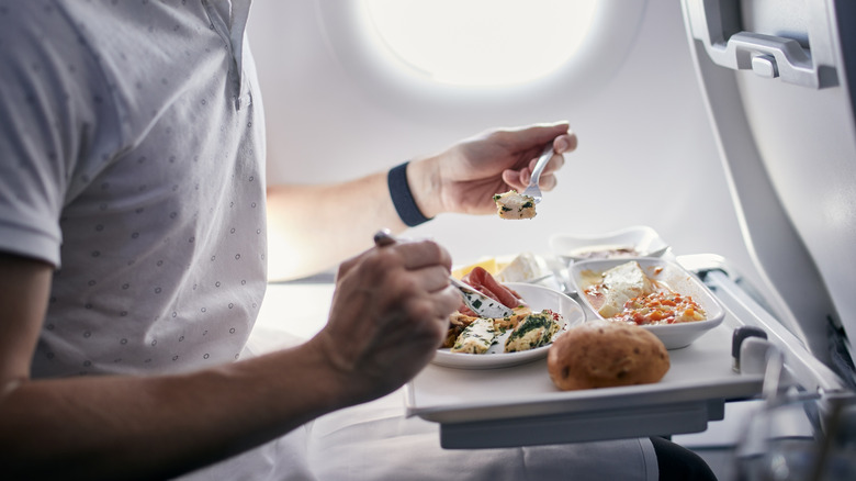 Close-up of a passenger eating an in-flight meal at his seat on an unidentified aircraft