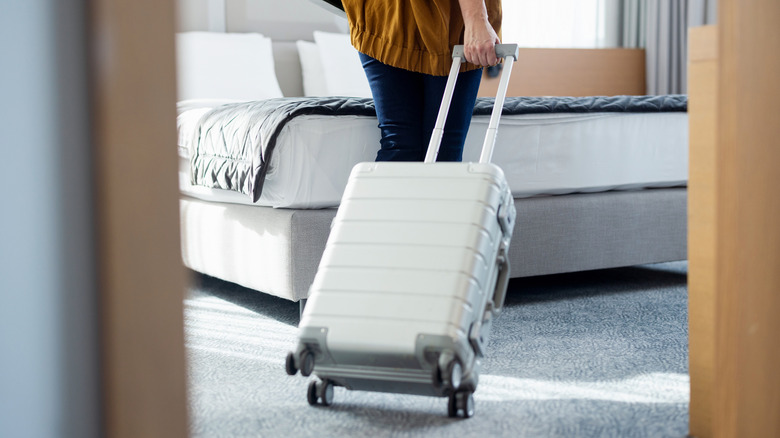 A traveler pulling a suitcase into a modern hotel room with a focus on the bed in the background