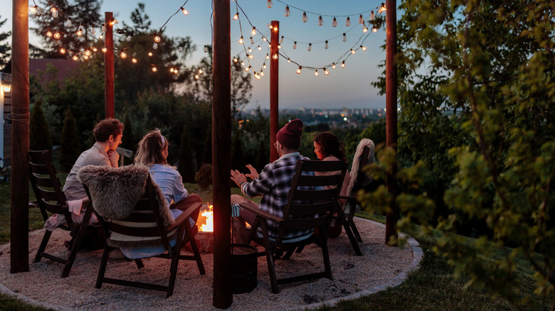 Group of people sitting in chairs around fire in the evening