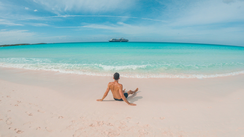 A man on a deserted beach on Half Moon Cay looking at his cruise ship