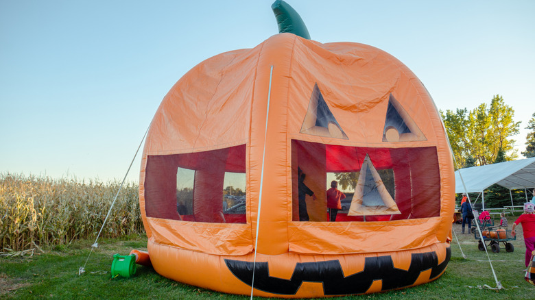 Pumpkin-shaped bounce house near corn field in Dayton, Minnesota with children bouncing inside during the day.