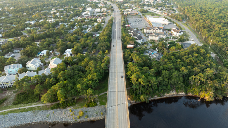 Long road cutting through lush green forests and the water, near Sea Breeze