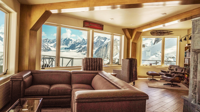 Interior view of the common area at Sheldon Chalet, a five-star luxury lodge located on a nunatak within the Don Sheldon Amphitheater in Denali National Park, Alaska, with views of the surrounding snow-covered peaks visible from the large windows.