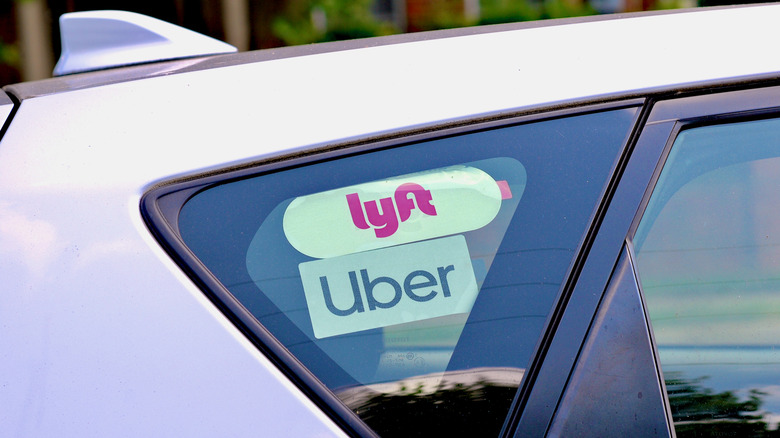 Silver car with Lyft and Uber stickers displayed in a window