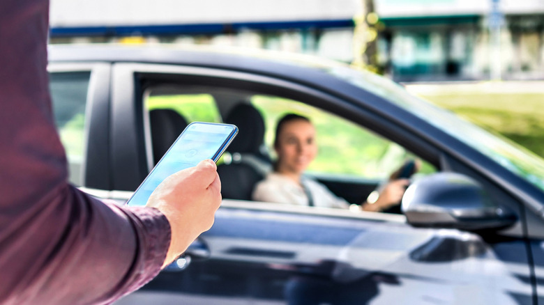 Person looking at a phone while a ride-share driver sits in her car