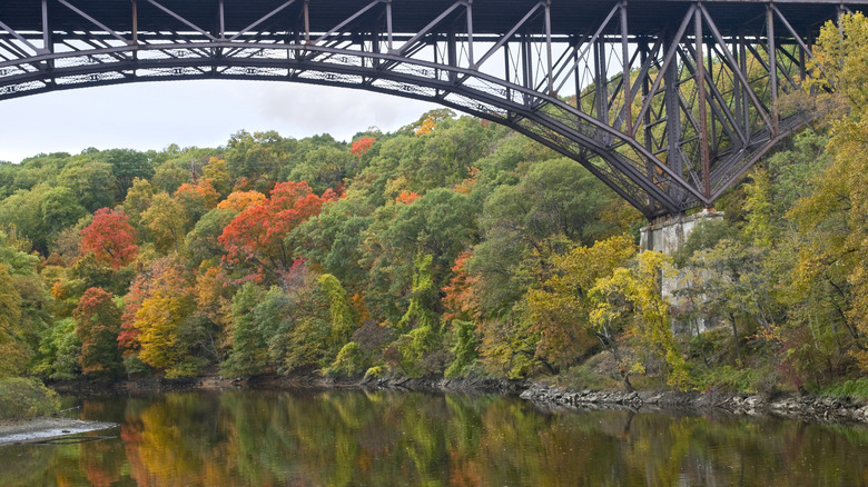 A bridge arches across Popolopen Creek as forests change colors during fall