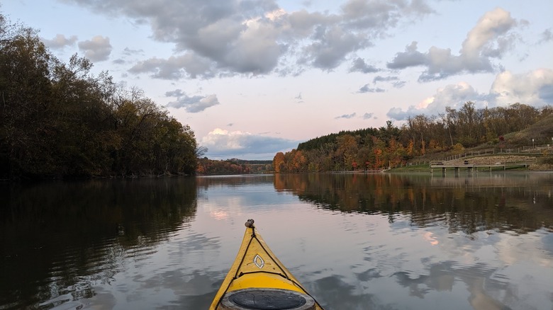 Cross Creek Lake in autumn, with a yellow kayak tip in the foreground on the water surrounded by fall trees with a wooden dock along the right side of the frame, under a cloudy sky at sunset