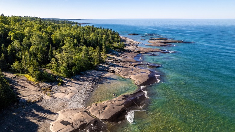 Trees line the shore of Lake Superior with sand and flat rocks
